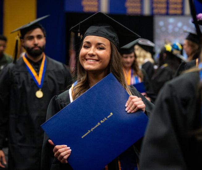 研究生 holds diploma in both hands and smiles at the camera, wearing graduation cap and gown.